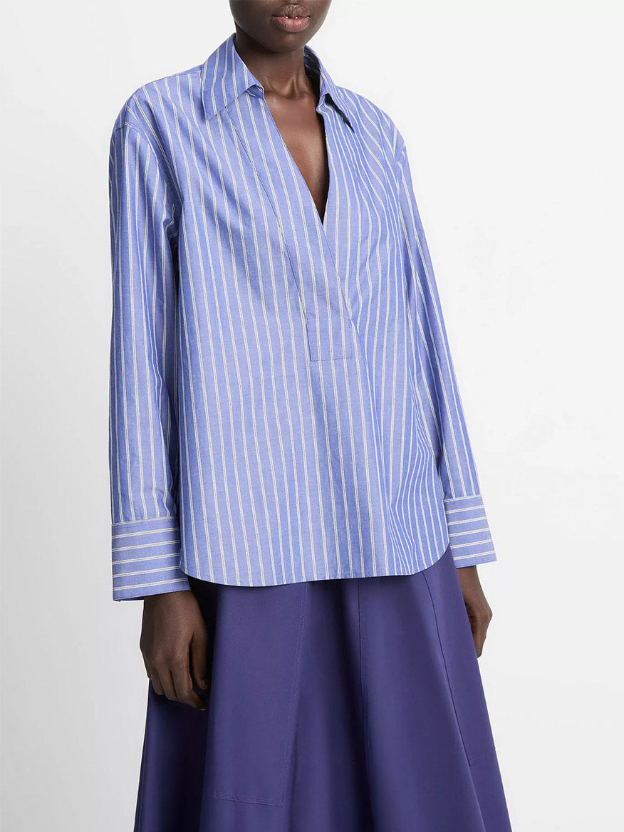 A person wearing the Vince Striped Cotton Relaxed Popover Shirt in Pale Twilight paired with a blue cotton poplin skirt.