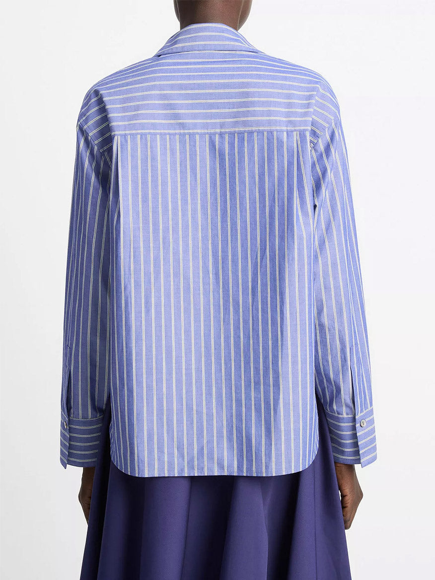 Person seen from the back wearing the Vince Striped Cotton Relaxed Popover Shirt in Pale Twilight—blue and white vertical stripes in breathable cotton poplin—paired with a dark blue skirt against a plain white background.