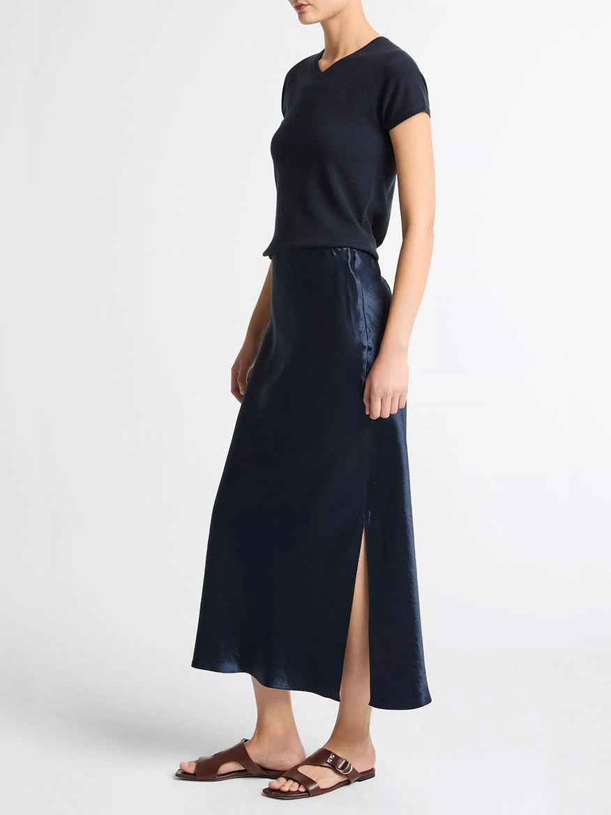 A person wearing a short-sleeve black top, the Vince Satin Side-Slit Slip Skirt in Coastal Blue, and brown sandals stands against a plain white background.