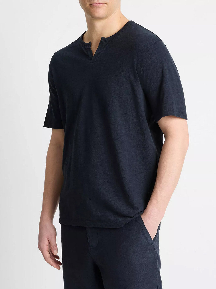 A man stands against a plain background, wearing the Vince Slub Cotton Split-Neck T-Shirt in Coastal Blue with matching pants, his hand casually in his pocket.