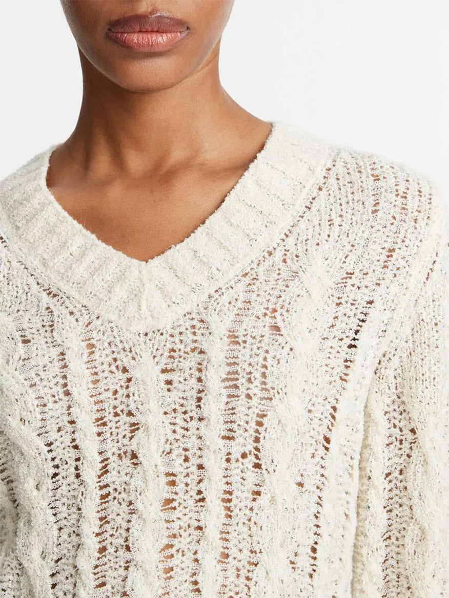 Close-up of a person wearing a Vince Textured Cable V-Neck Sweater in Cream with an open-knit design and a v-neck.