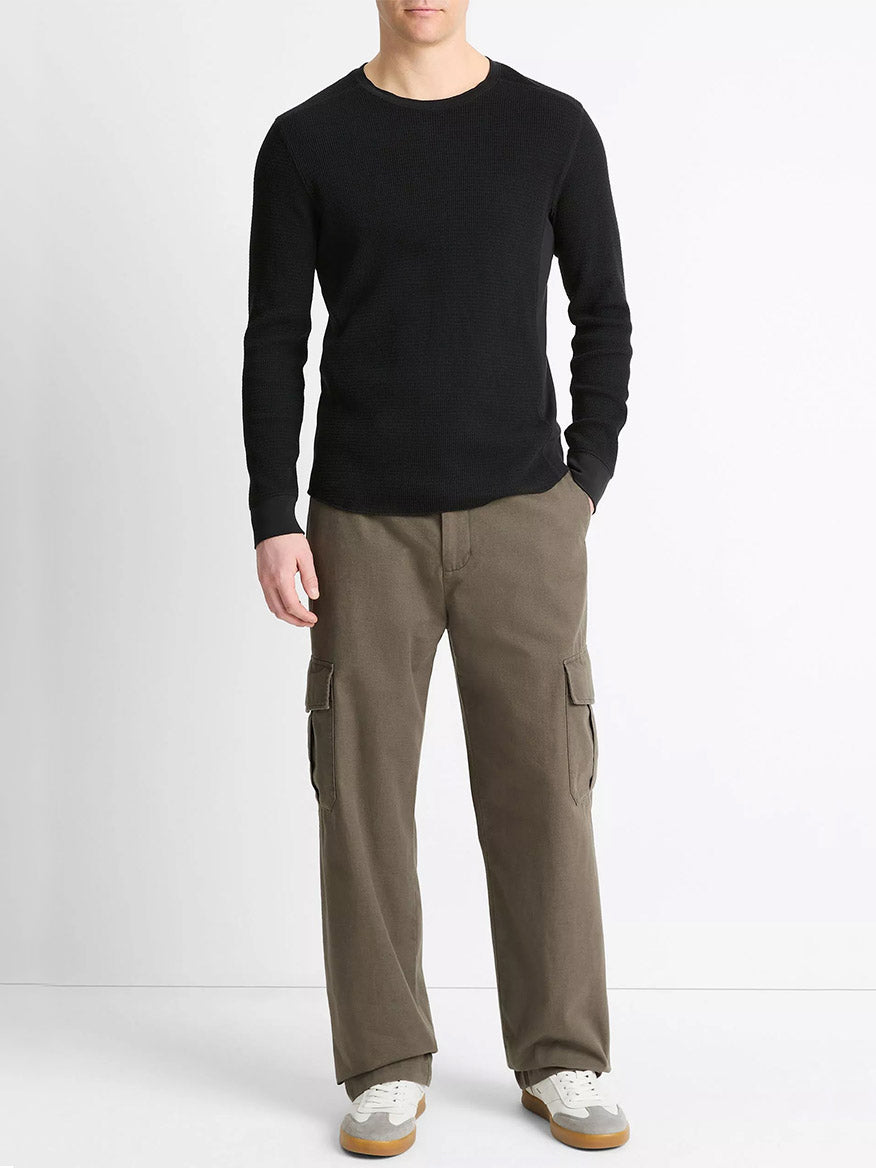 A person wearing a Vince Pima Cotton-Blend Thermal Long-Sleeve Pullover in black, brown cargo pants, and white sneakers stands against a plain white background.