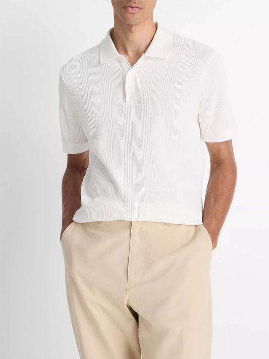 A man stands with hands in pockets, wearing the Vince Variegated Pima Cotton Polo Shirt in Off White and beige trousers against a plain background.
