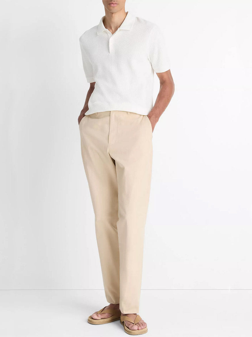 A person wears the Vince Variegated Pima Cotton Polo Shirt in Off White, paired with beige pants and tan sandals, standing against a plain white background with hands in pockets.
