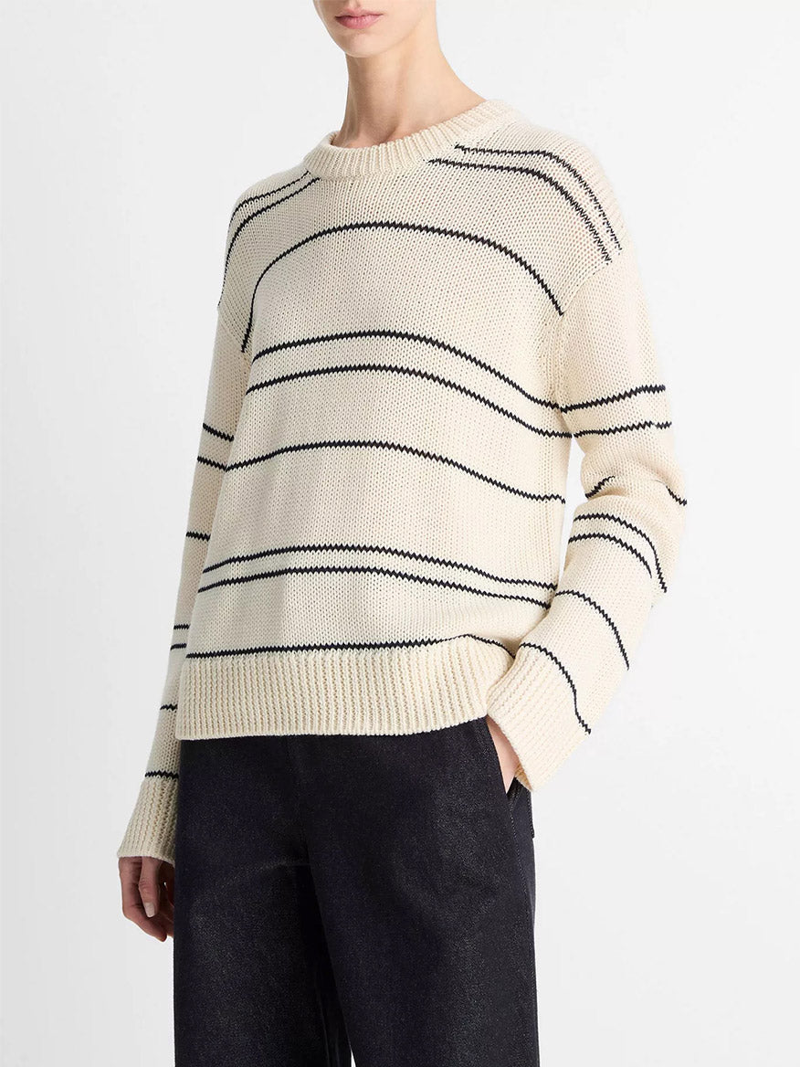 A person wearing the Vince Variegated Stripe Wool-Blend Sweater in Oat Shell/Navy with dark pants, standing against a plain background.