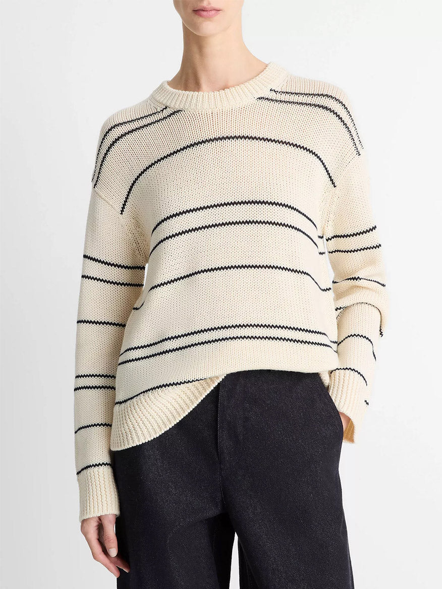 A person wears the Vince Variegated Stripe Wool-Blend Sweater in Oat Shell/Navy with black pants, standing against a plain white background.