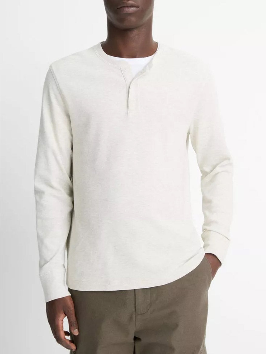 A person wears the Vince Pima Cotton Waffle Henley in Heather Baja Sand—crafted from soft Peruvian Pima cotton—with brown pants, standing against a plain background.