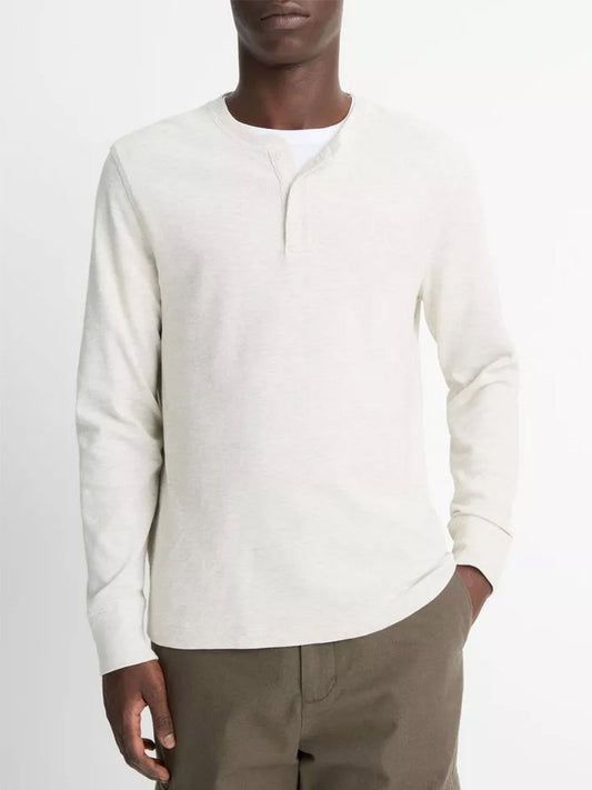 A person wears the Vince Pima Cotton Waffle Henley in Heather Baja Sand—crafted from soft Peruvian Pima cotton—with brown pants, standing against a plain background.