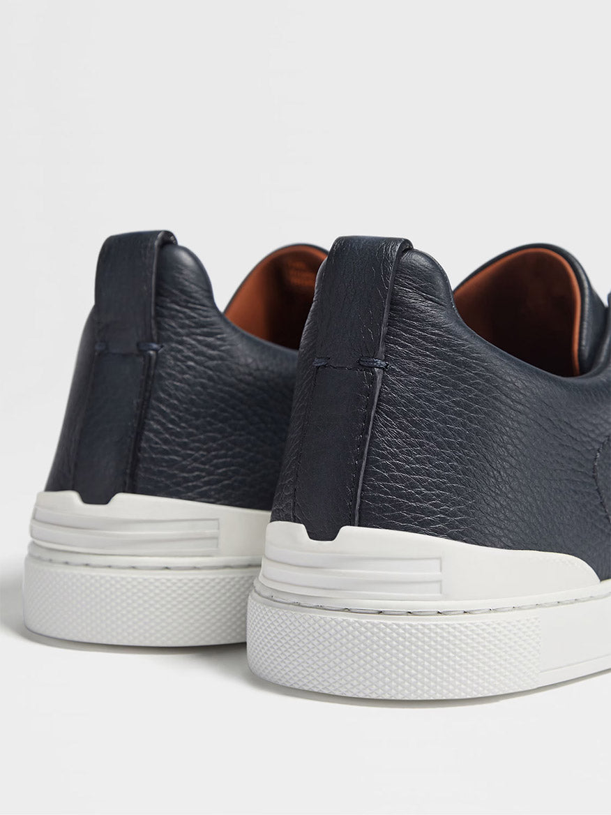 Close-up of the back view of Zegna Navy Blue Deerskin Triple Stitch™ Sneakers featuring white rubber soles on a plain background.
