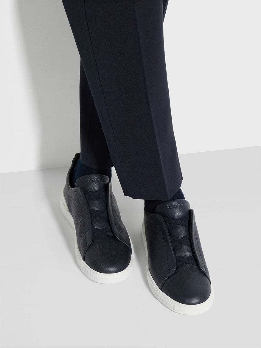 A person wearing Zegna Navy Blue Deerskin Triple Stitch™ Sneakers.