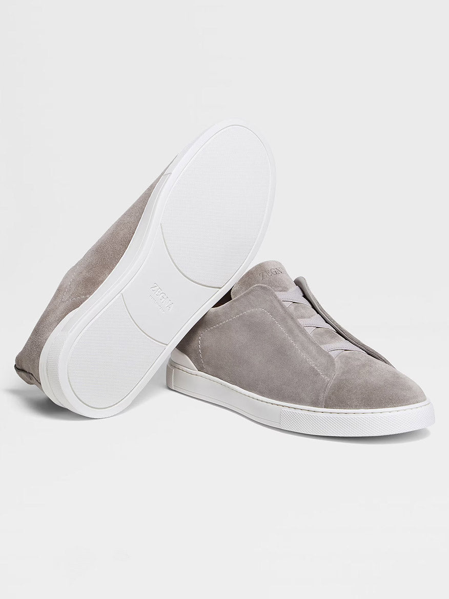 The Zegna Light Grey Suede Triple Stitch™ Sneakers feature lightweight suede and white rubber soles, beautifully displayed with one upright and the other on its side to showcase their fine craftsmanship.