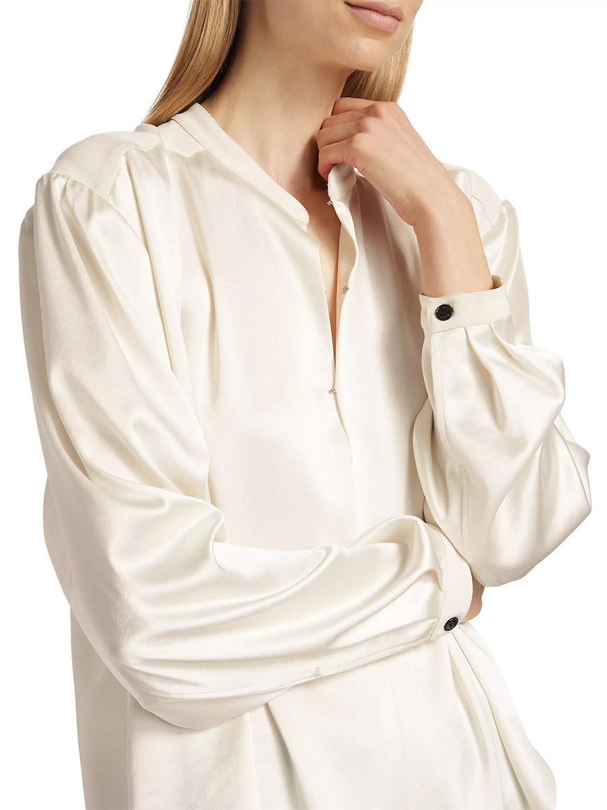 A woman in a rag & bone Rosie Keyhole Blouse in Ivory with puffed sleeves and buttoned cuffs, standing with her arms crossed.