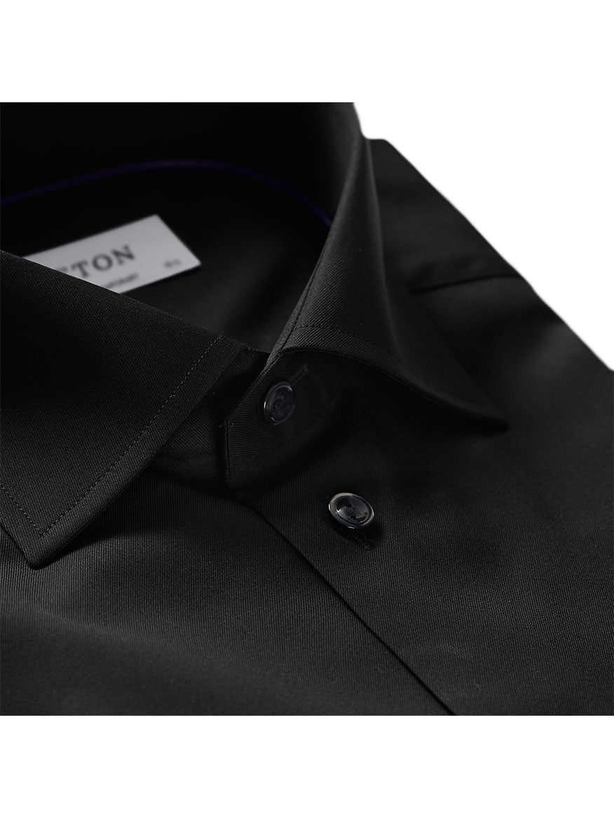 A close-up of a black business shirt with a turndown collar and two black buttons. The contemporary fit and wrinkle-free fabric make it perfect for long days at the office. A label inside the collar reads "Eton Contemporary Fit Black Signature Twill Dress Shirt.