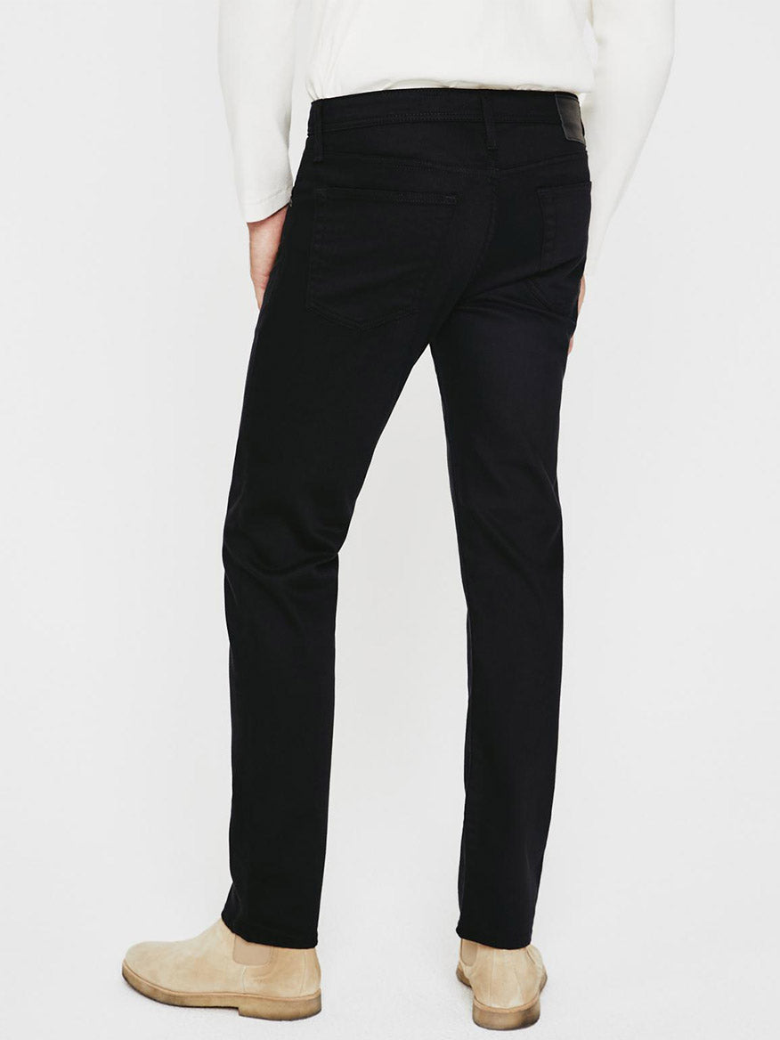 The back view of a man wearing black jeans, specifically the AG Jeans Tellis in Fathom in a modern slim fit.