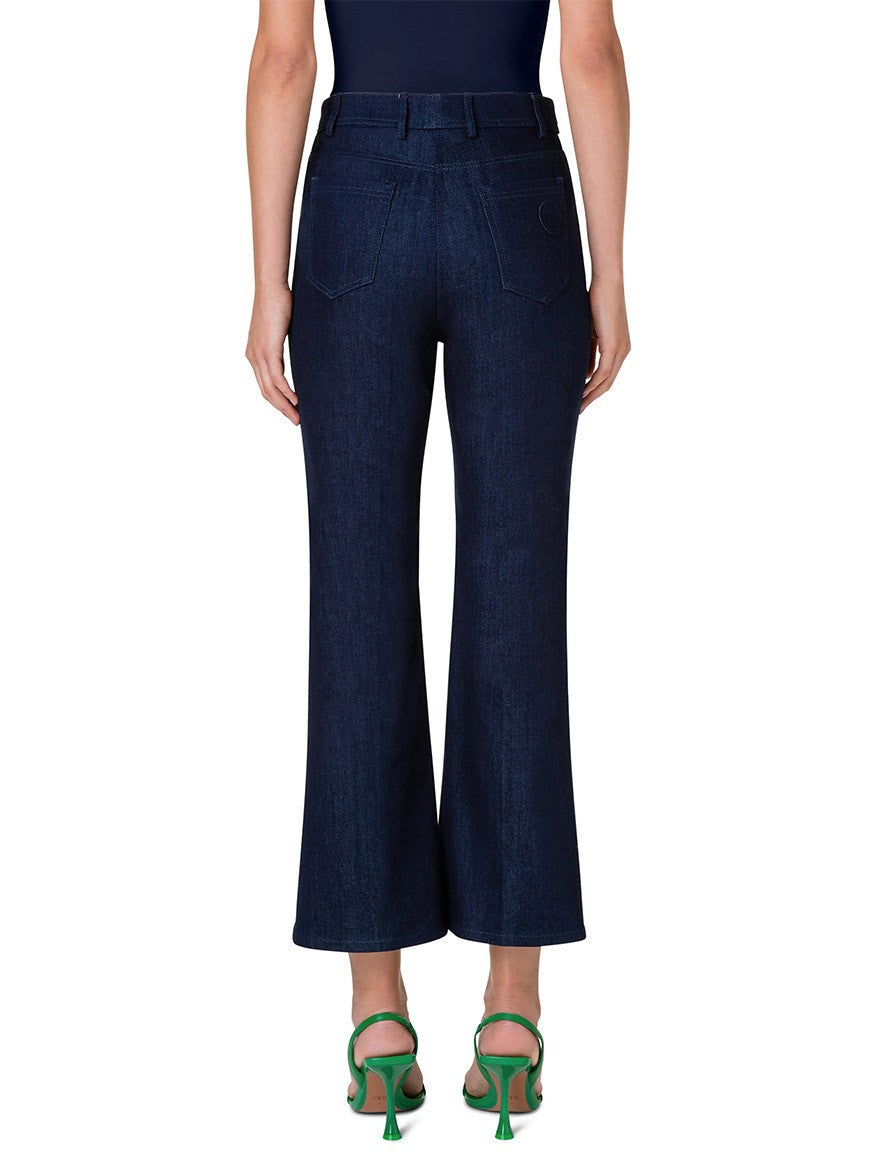 Rear view of a person wearing Akris Punto Cali Stretch Crop Bootcut Denim in Dark Blue and green heeled sandals, standing against a white background.