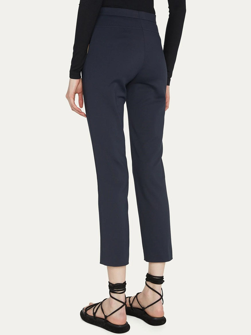 A person wearing Akris Punto Franca Mid-Rise Ankle Pants in Navy paired with a black top and black strappy sandals is shown from the back.