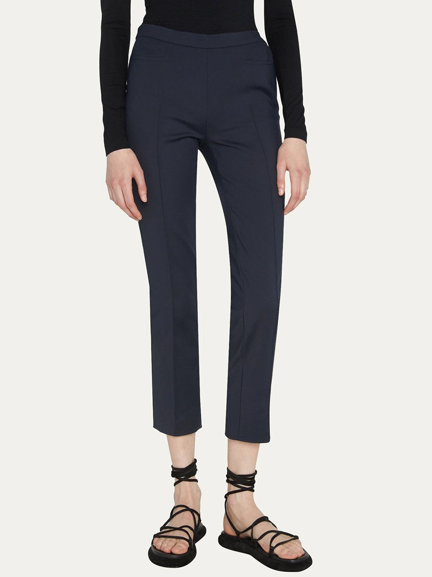 Person wearing a long-sleeve black shirt, Akris Punto Franca Mid-Rise Ankle Pants in Navy with slim-cut legs, and black strappy sandals.