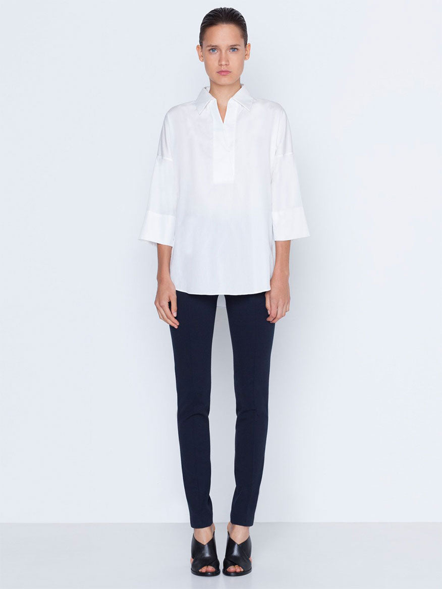 A person standing against a plain background wearing a white shirt, Akris Punto Mara Stretch Jersey Pants in Navy with front zip closure, and black shoes.