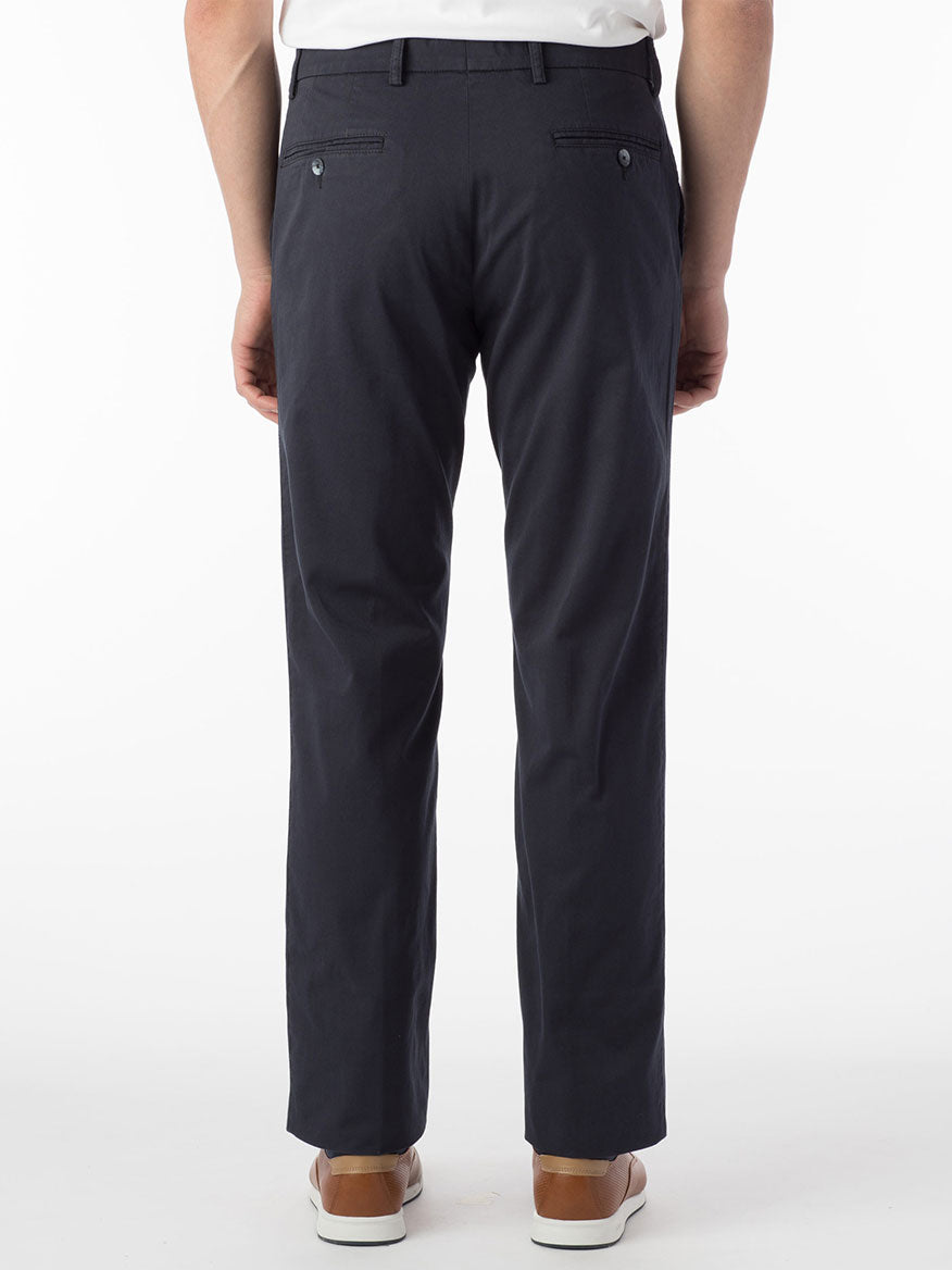Rear view of a person wearing Ballin Atwater True Khaki Modern Flat Front Pants in Navy, a white Pima cotton shirt, and brown shoes, standing against a plain white background.