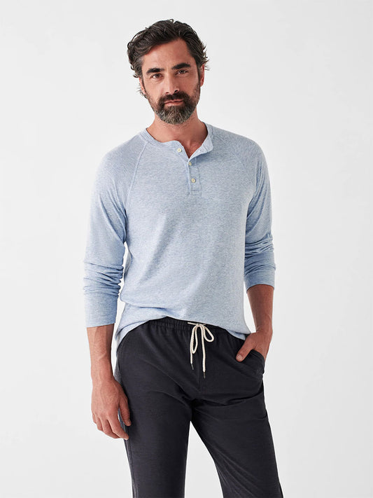 Man posing in a Faherty Brand Cloud Long-Sleeve Henley in Light Blue Heather and black drawstring trousers.
