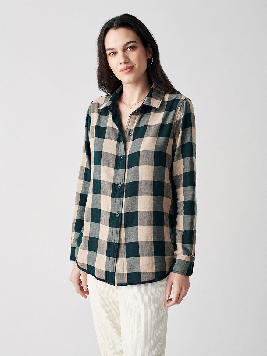 Woman in Faherty Brand Classic Reversible Shirt in Blackwatch and white pants standing against a plain background.