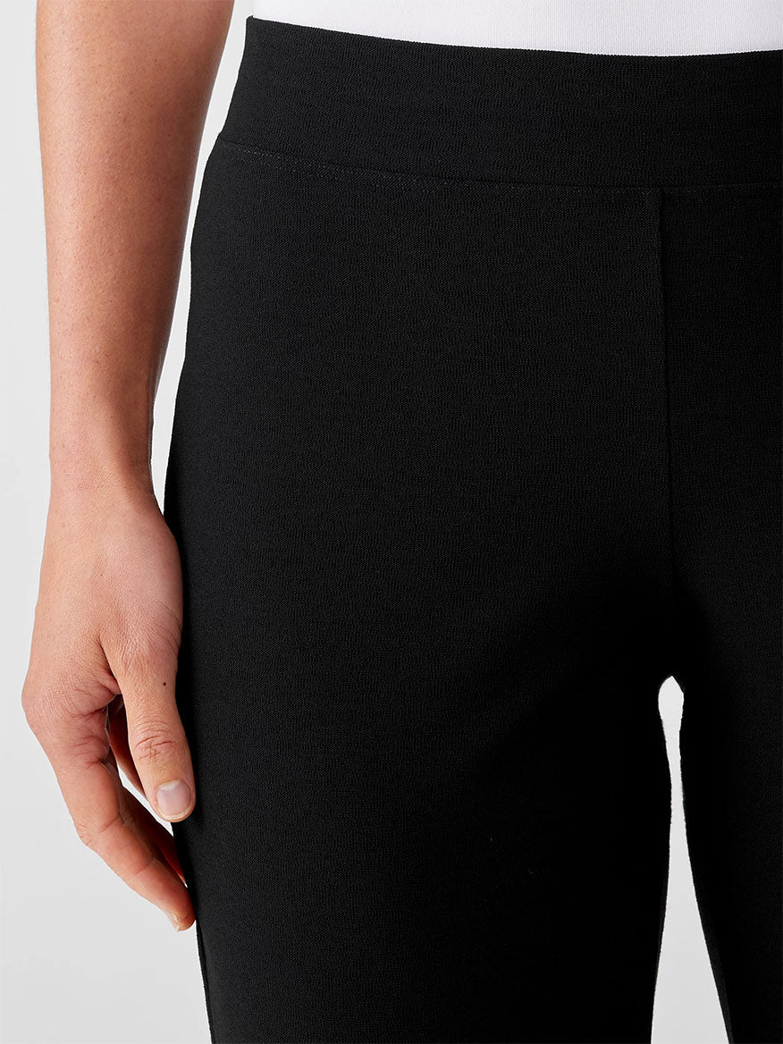 Close-up of a person's hand resting on the hip area of a black Eileen Fisher Washable Stretch Crepe Pant, made from stretch crepe fabric.