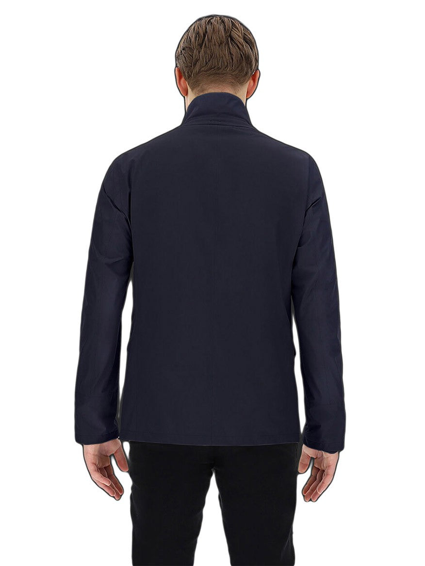 Man standing with his back to the camera, wearing a dark, waterproof Herno Laminar Blazer in Navy and black pants.