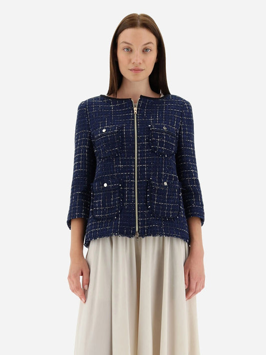 A woman stands wearing a Herno Jacket in Casual Tweed in New Blue, complete with practical pockets, paired with a cream skirt against a plain background.