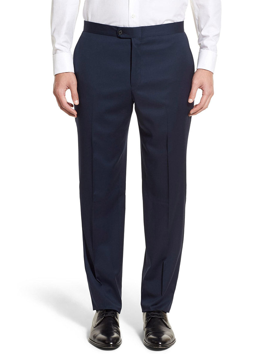 A person in elegant navy dress pants and a crisp white shirt, perfectly complementing the Peak Lapel of the Hickey Freeman (Heritage Gold) Navy Tasmanian Wool Tuxedo, stands with arms at sides, wearing sophisticated black shoes.