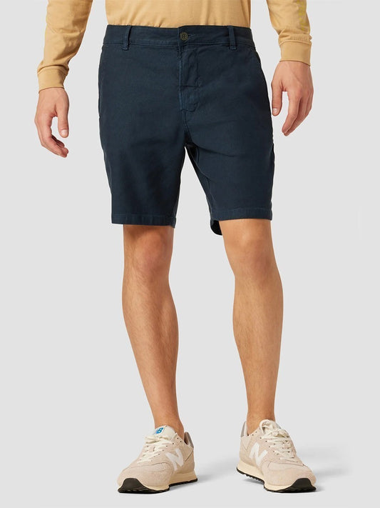 A person wearing navy blue Hudson Chino Shorts in Night Blue and beige sneakers standing against a neutral background.