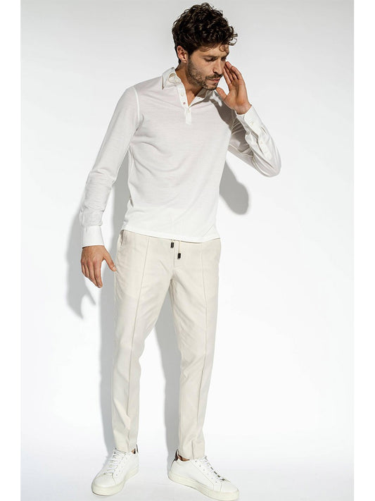 A person wearing an Isaia Evening Polo in White, beige pants, and white sneakers, all impeccably crafted by Isaia and Made in Italy, stands against a plain white background.
