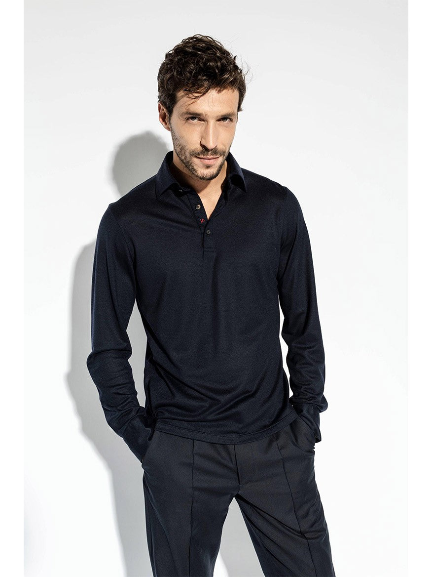 A man with short hair and facial hair is wearing an Isaia Evening Polo in Navy and pants. His hands are in his pockets, and he is standing against a plain white background.