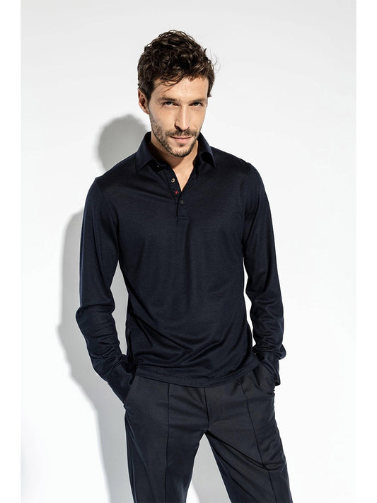 A man with short hair and facial hair is wearing an Isaia Evening Polo in Navy and pants. His hands are in his pockets, and he is standing against a plain white background.