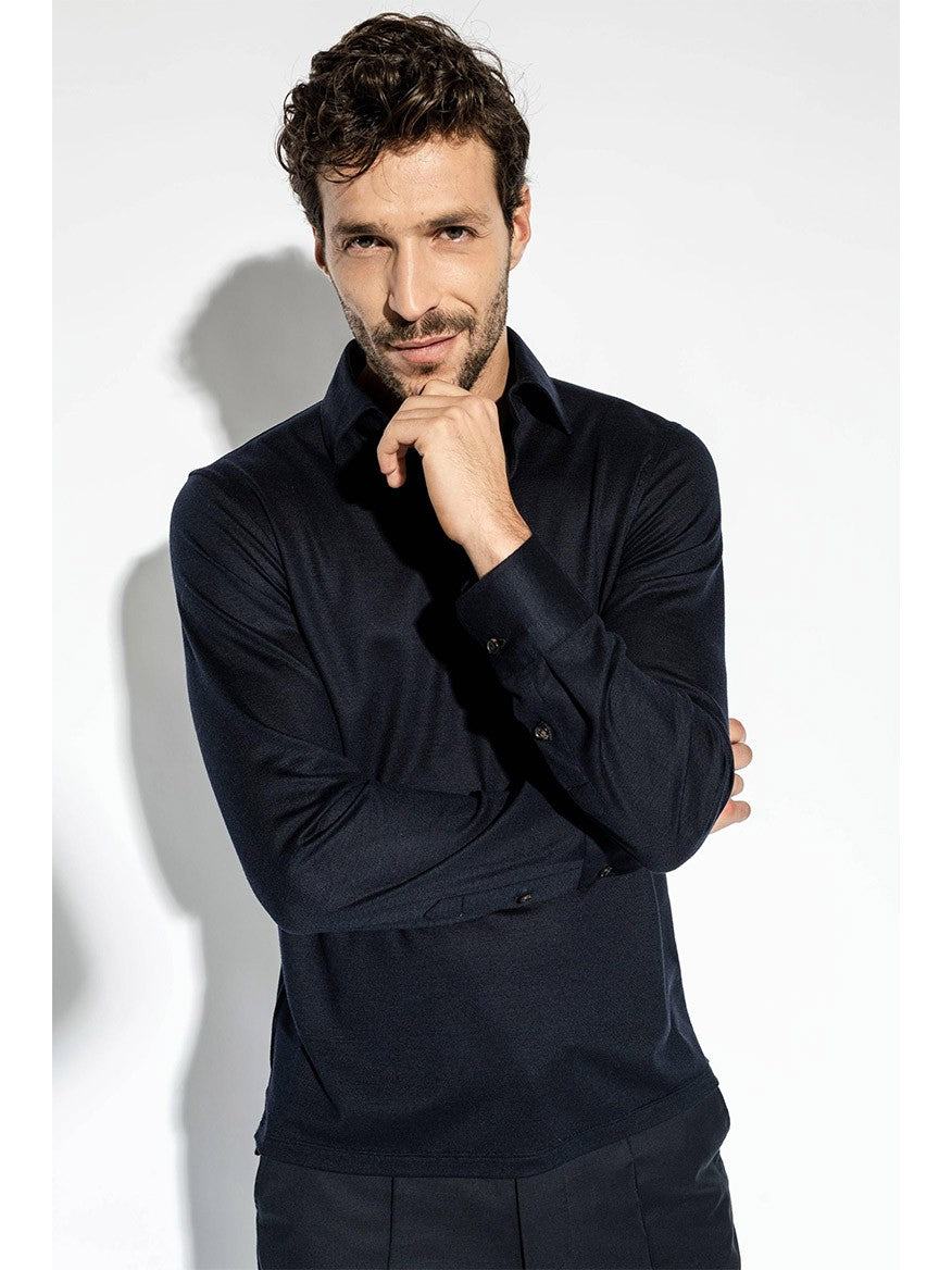 A man with short, curly hair and a beard is wearing an Isaia Evening Polo in Navy. He is posing with his right hand touching his chin and his left arm crossed over his body.