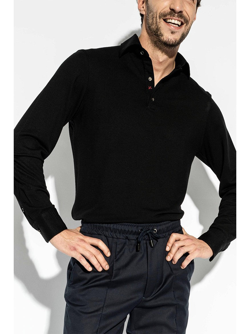 A man wearing an Isaia Evening Polo in Black and dark blue pants stands with his hands on his hips, smiling.