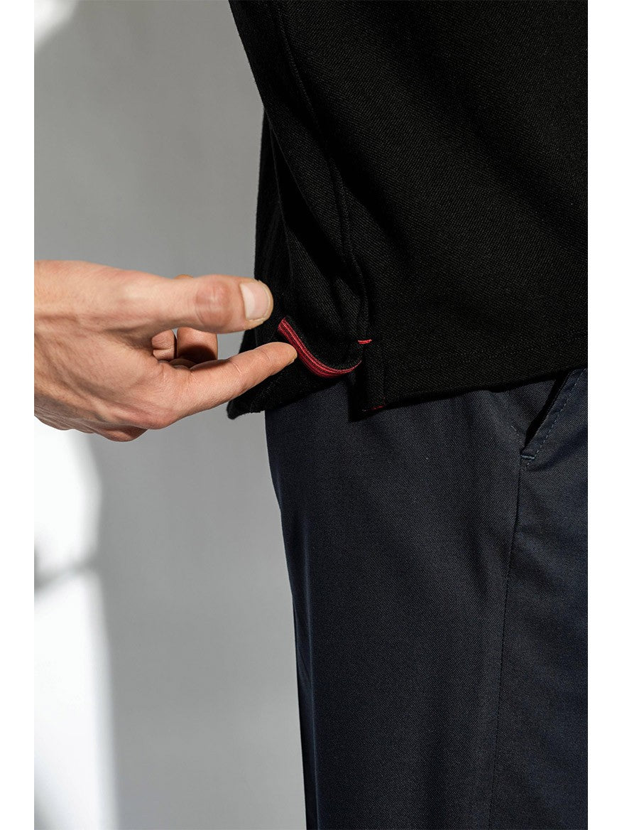 A person pulling a small red loop on the hem of a black garment, demonstrating an adjustment feature, while dressed in dark pants and an Isaia Evening Polo in Black.