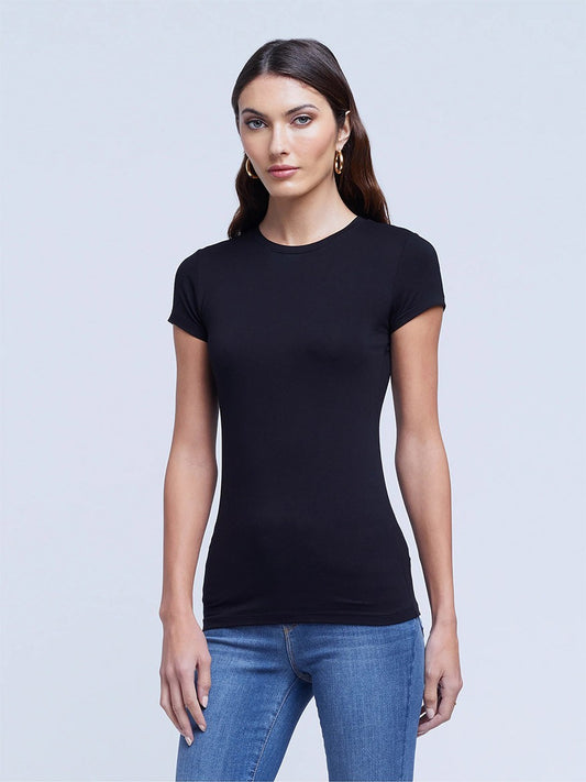 Woman in a L'Agence Ressi Short Sleeve Crew in Black and jeans standing against a plain gray background, looking directly at the camera.