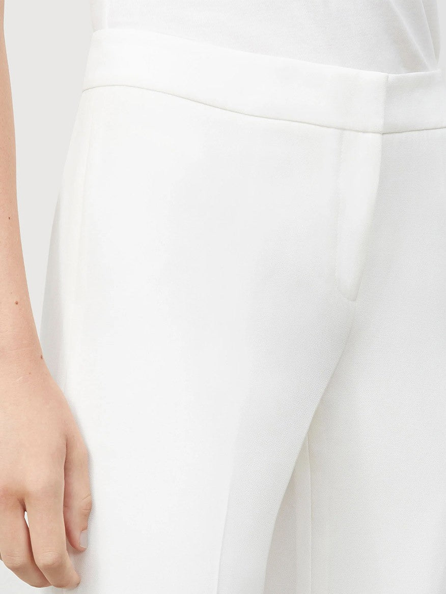 Person wearing white Lafayette 148 New York Finesse Crepe Barrow Pant in Cloud and a white top, with a close-up focus on the expertly tailored trousers' waist and upper leg.