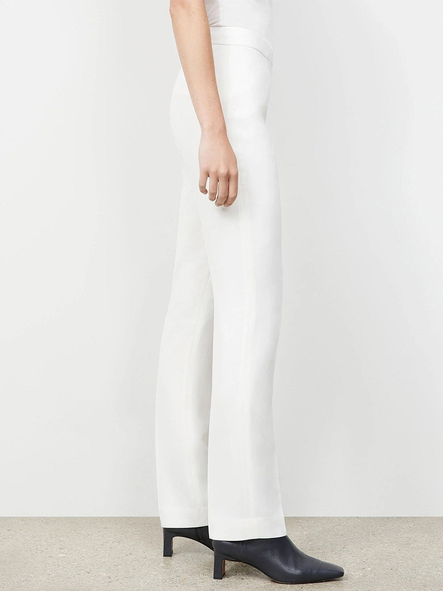 Person wearing expertly tailored white high-waisted Lafayette 148 New York Finesse Crepe Barrow Pant in Cloud and black ankle boots, standing sideways against a plain background.
