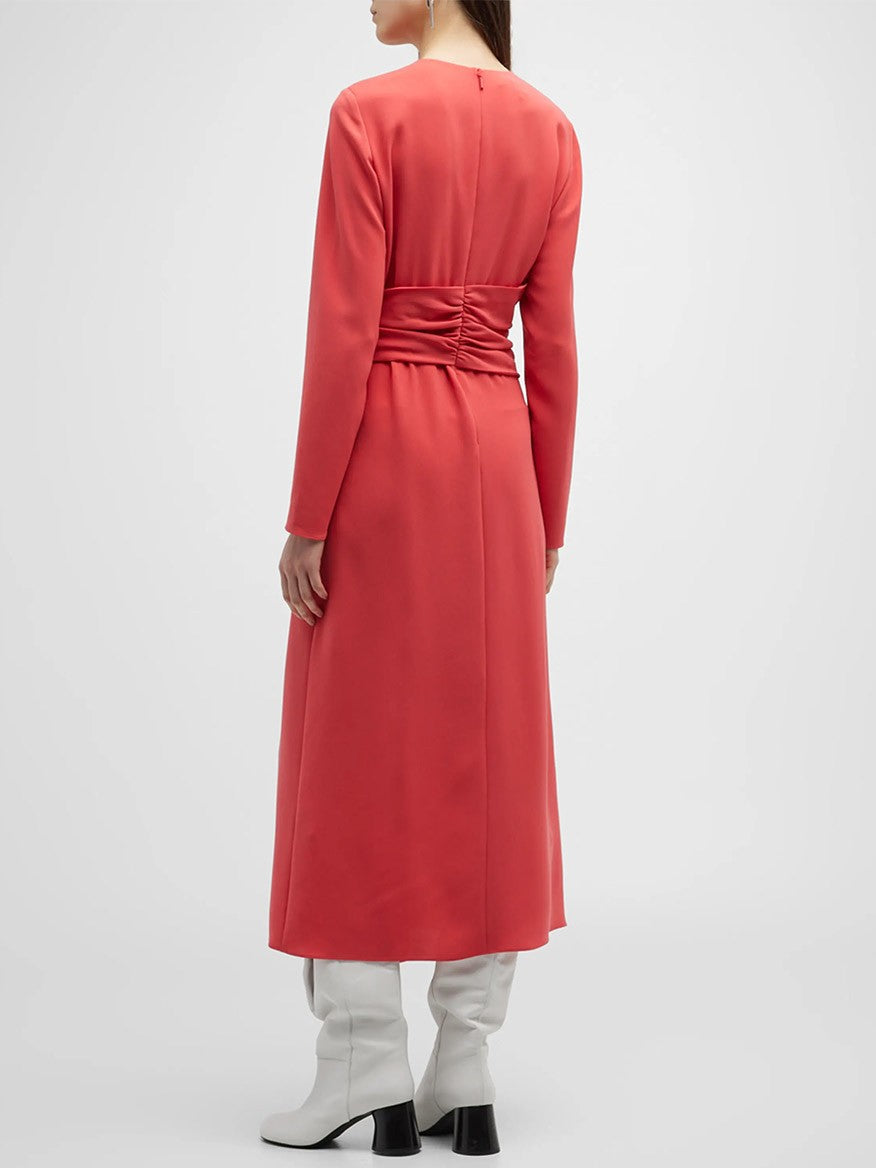 A person wearing a Lafayette 148 New York Finesse Crepe Twist Dress in Coral, featuring an A-line silhouette, coral-colored with a cinched waist and white heeled boots, viewed from the back.