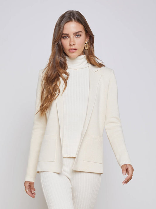 A woman in a white turtleneck and L'Agence Lacey Knit Blazer in Porcelain poses against a gray background.