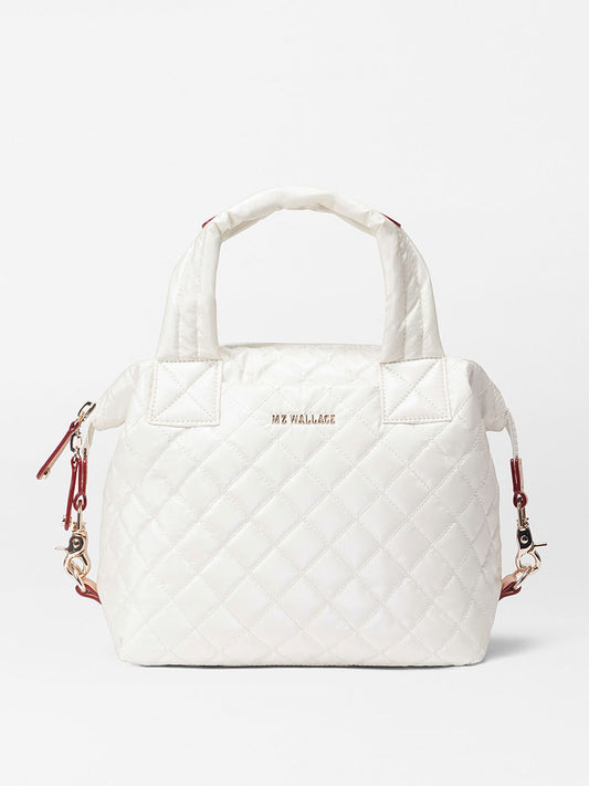 White quilted MZ Wallace Small Sutton Deluxe in Pearl Metallic Oxford tote bag with diamond stitching, featuring short handles, a zipper closure, red accents, and a crossbody strap. Logo displayed in the center.