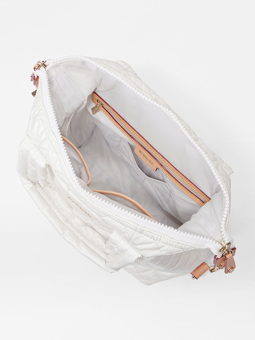 MZ Wallace Small Sutton Deluxe in Pearl Metallic Oxford open to show a spacious interior with multiple pockets, including exterior pockets and a zipper compartment, set against a plain background.