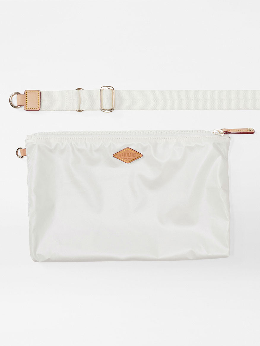 A MZ Wallace Small Sutton Deluxe in Pearl Metallic Oxford waist pouch with an adjustable beige crossbody strap and metallic buckles, featuring a small, brown logo patch on the front.