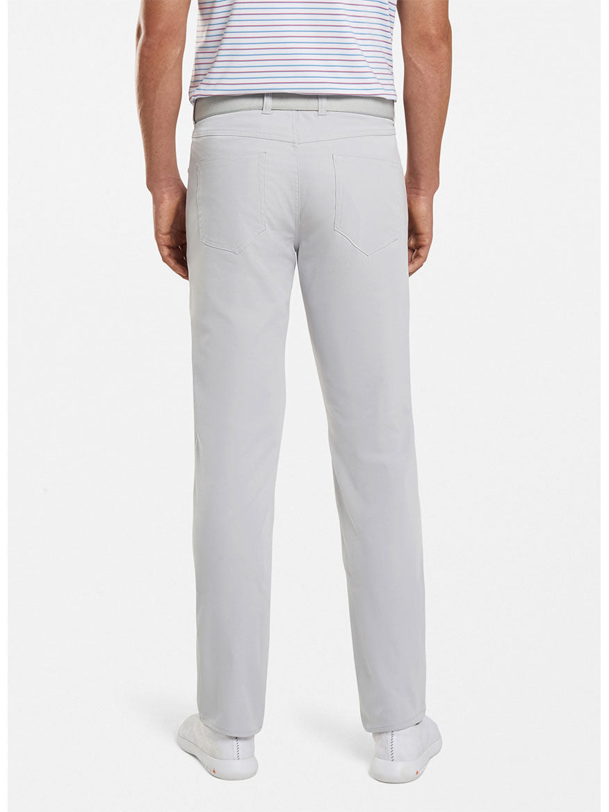 Back view of a person wearing Peter Millar Performance Five-Pocket Pant in British Grey, a tucked-in short-sleeve striped shirt, and white shoes.