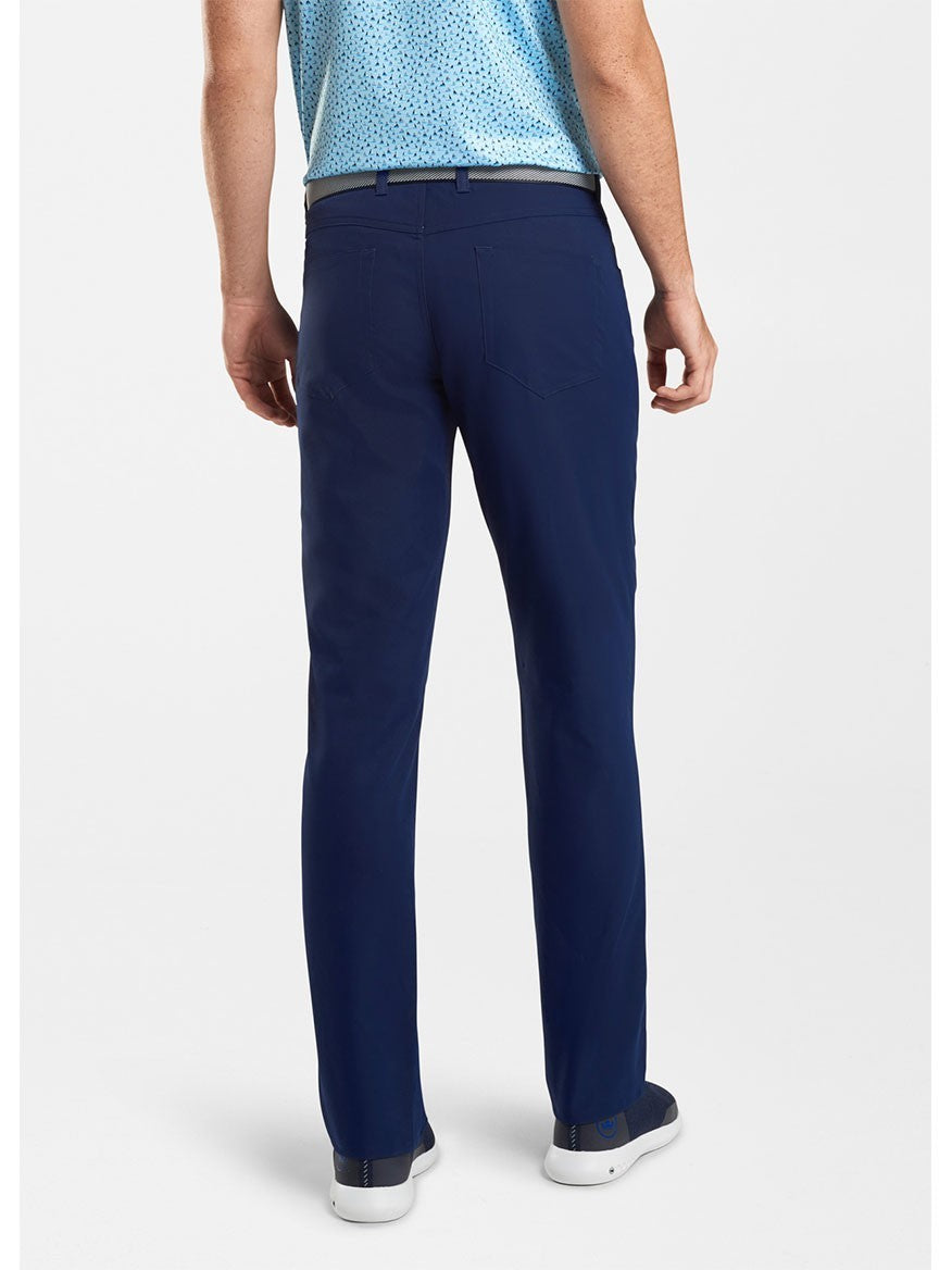 A person is standing with their back facing the camera, wearing a blue short-sleeve shirt, Peter Millar Performance Five-Pocket Pant in Navy, and blue sneakers.