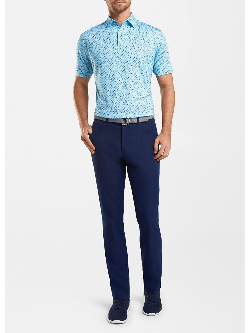 A person standing and wearing a light blue patterned polo shirt, Peter Millar Performance Five-Pocket Pant in Navy, a black belt, and navy blue shoes, against a plain white background. This outfit is similar to what PGA Tour players might wear on the course.