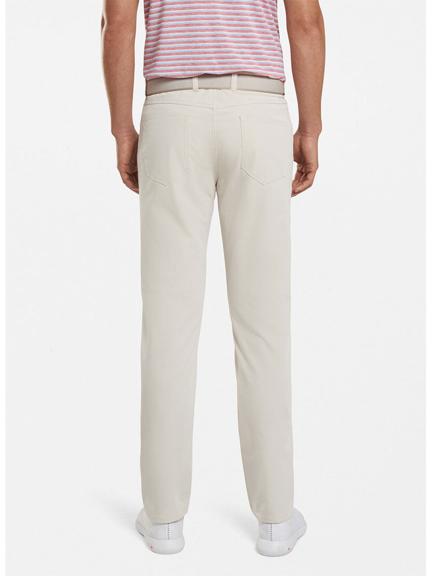 Rear view of a man wearing Peter Millar Performance Five-Pocket Pant in Stone and white sneakers, paired with a striped pink and white t-shirt.