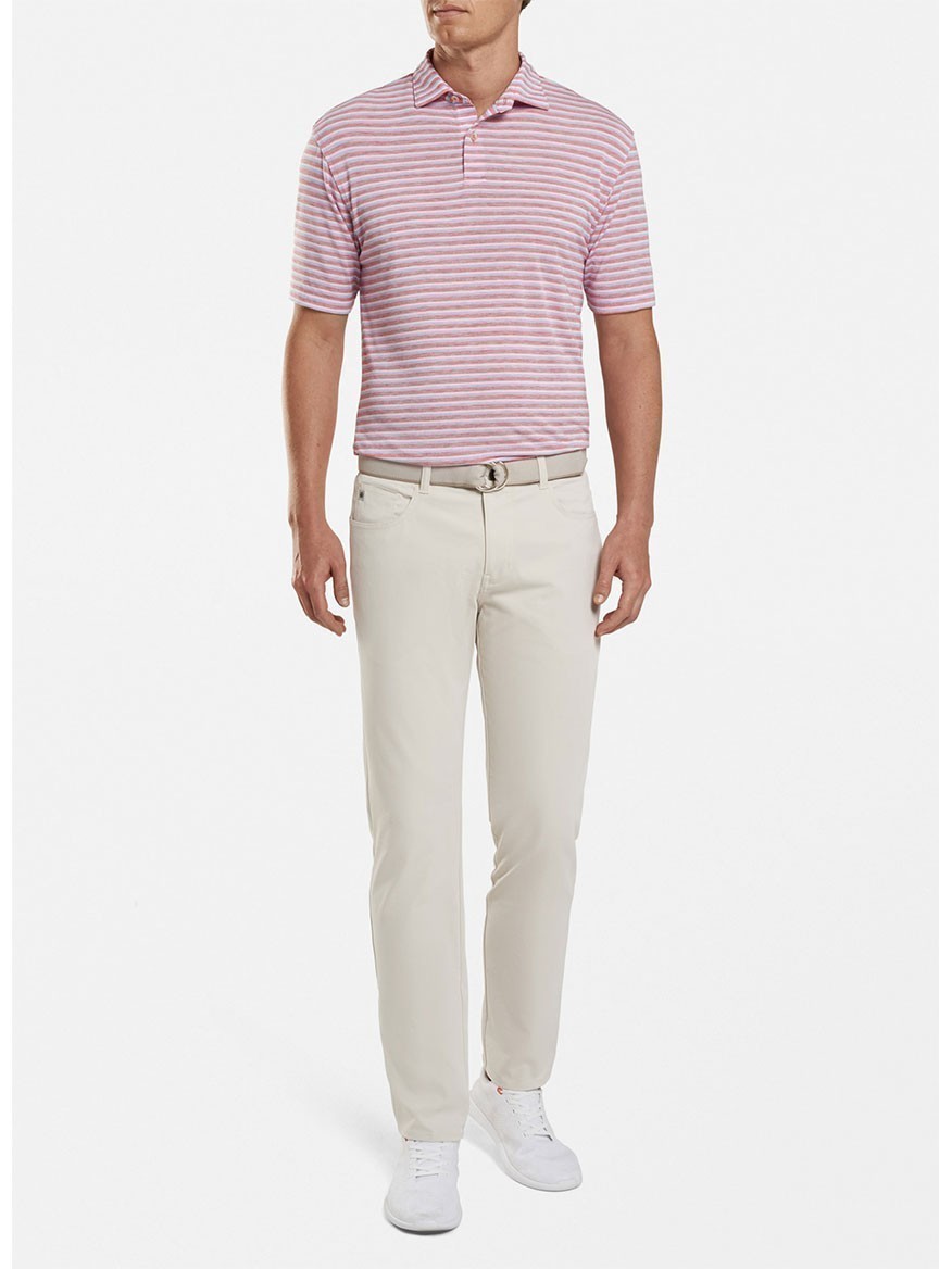 A man wearing a pink-striped polo shirt and Peter Millar Performance Five-Pocket Pant in Stone paired with white sneakers, standing against a plain background.