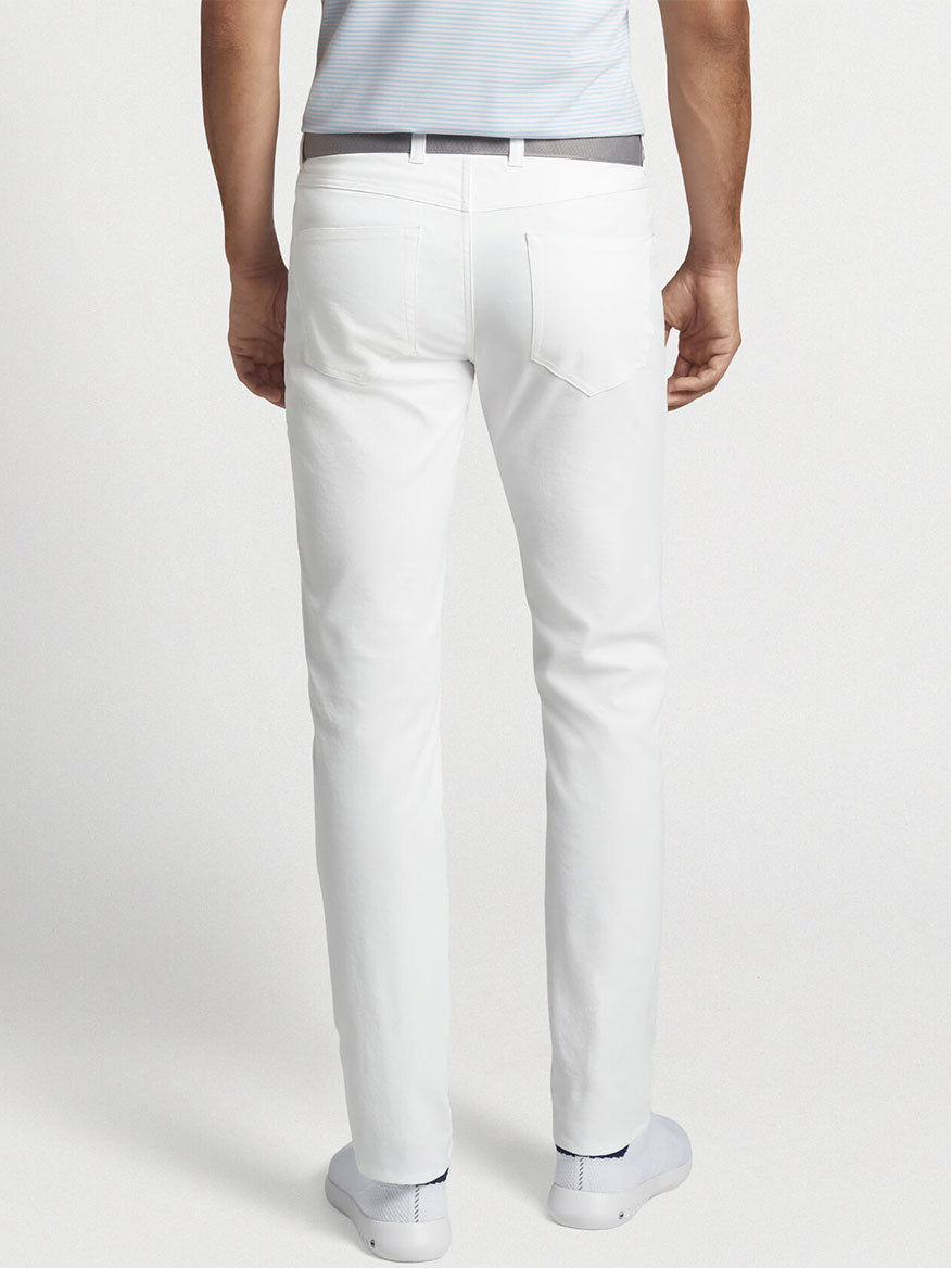 Back view of a person dressed in a light blue shirt and white shoes, showcasing stylish Peter Millar Performance Five-Pocket Pants in White, crafted with two-way stretch for ultimate comfort.